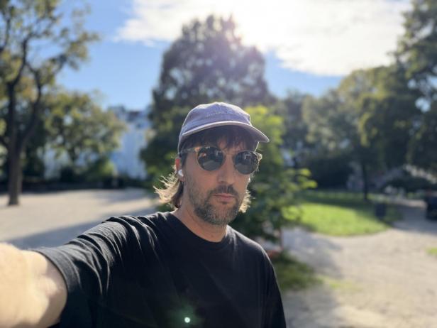 Mann mit Sonnenbrille und Kappe macht ein Selfie im Park.
