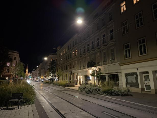 Eine Straßenbahnhaltestelle in einer belebten Straße bei Nacht.