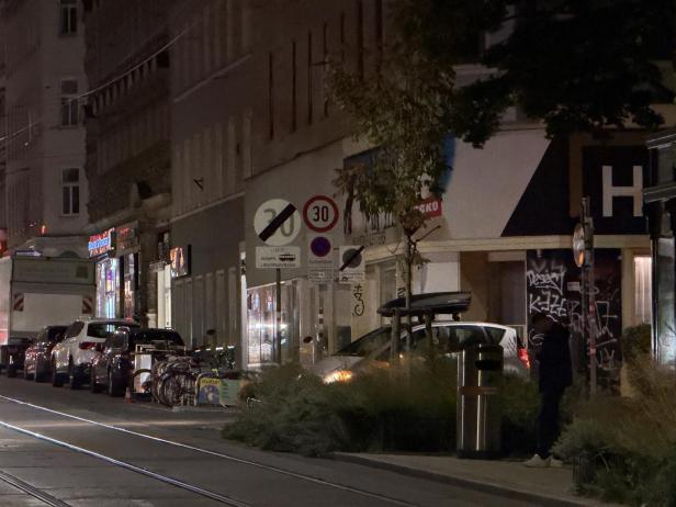 Eine abendliche Straßenszene mit geparkten Autos und einer Straßenbahnhaltestelle in Wien.