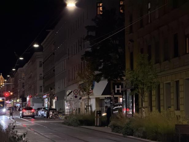 Eine abendliche Straßenszene mit Autos, einer Straßenbahn und Passanten.
