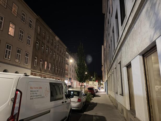 Eine abendliche Straßenszene in Wien mit parkenden Autos und einem Lieferwagen von „Bau Tischler Jako“.