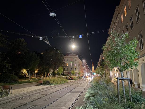 Eine Straßenbahnhaltestelle in einer Stadt bei Nacht, aufgenommen im Nachtmodus.
