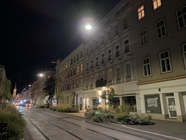 Eine abendliche Straßenszene in Wien mit Straßenbahnschienen und beleuchteten Gebäuden.