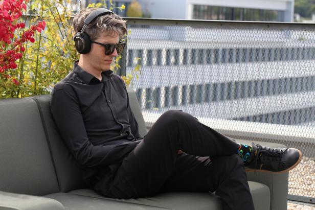 Ein Mann mit Kopfhörern und Sonnenbrille sitzt auf einer Couch.