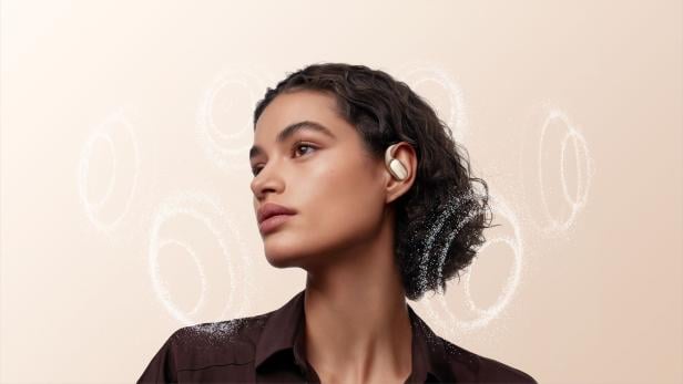 Eine Frau mit braunen Locken trägt goldene Xiaomi Open Wear Stereo Pro Ohrhörer.