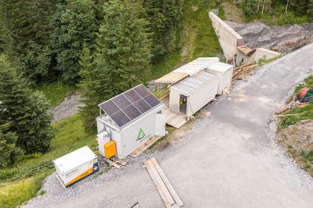 Mobiler Batteriespeicher mit Solarpanels und Containern auf einer Baustelle im Gebirge.