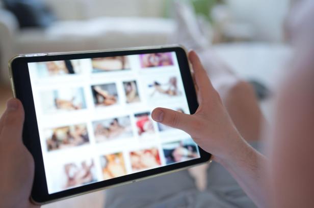 Eine Person hält ein Tablet mit einer geöffneten Pornoseite in der Hand.