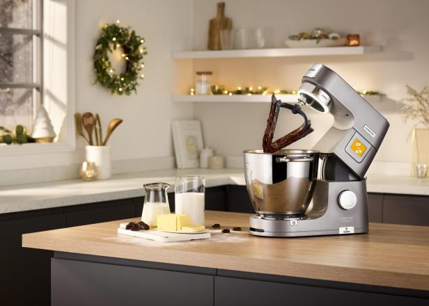 Eine Küchenmaschine mit Schokoladenteig steht auf einer Arbeitsplatte, daneben liegen Butter, Milch und Schokolade bereit.