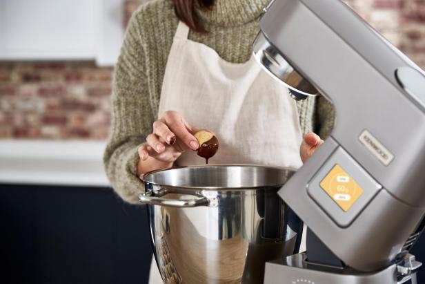 Eine Person taucht ein Gebäckstück zur Hälfte in flüssige Schokolade über einer großen Rührschüssel.