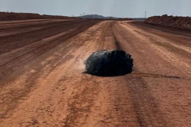 Ein verkohltes, rauchendes Objekt liegt auf einer staubigen Wüstenstraße, vermutlich ein aus dem All stammendes Trümmerteil.