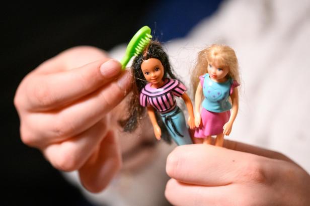 Eine Hand hält zwei kleine Puppen, einer wird mit einem grünen Kamm die Haare gekämmt.