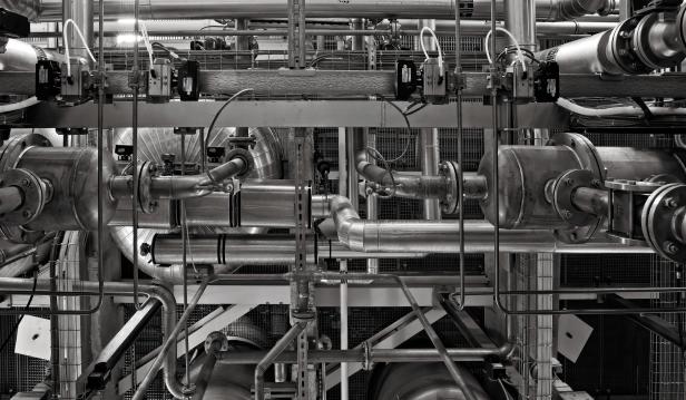 Schwarz-weiße Aufnahme eines komplexen Rohrleitungssystems mit Ventilen, Halterungen und Kabeln in einer Industrieanlage.
