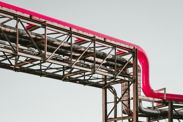 Pinkes Rohr auf einem Stahlgerüst vor hellem Himmel, das sich in einem rechten Winkel nach unten biegt.
