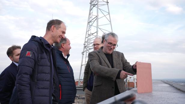 mehrere Männer blicken im Freien auf ein Tablet