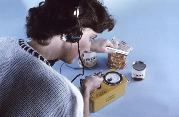 Frau misst mit einem Geigerzähler die Strahlung von Konservendosen und Lebensmitteln.