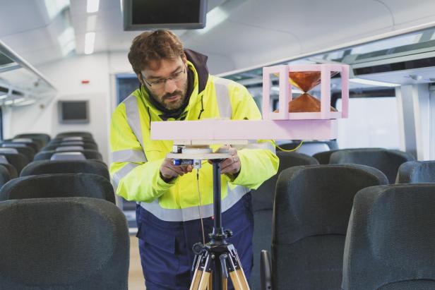 ein Mann in neongelber Jacke mit einem Versuchsaufbau in einem Zug