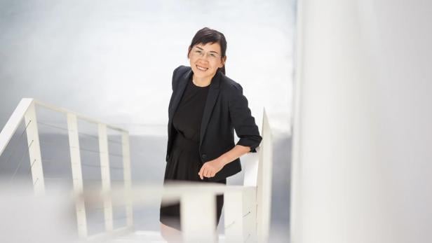 eine Frau in schwarzem Outfit geht eine Treppe nach oben und lächelt in die Kamera