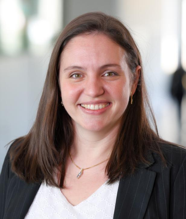 Frau mit braunen Haaren und weißer Bluse lächelt in die Kamera.