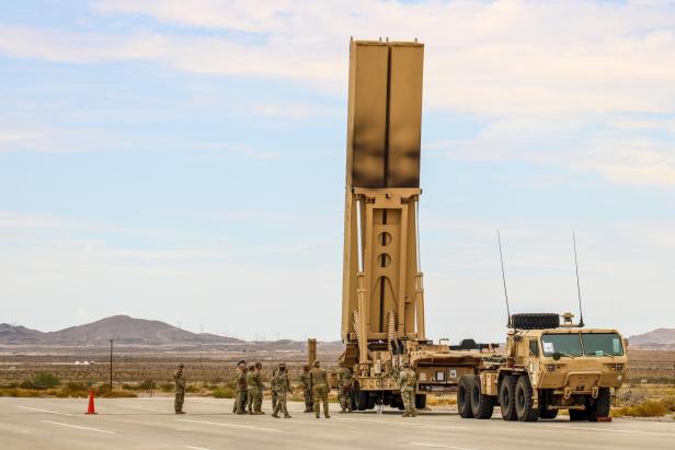 Soldaten stehen neben einem Lkw mit aufgerichtetem Raketenstartsystem in Wüstenlandschaft.