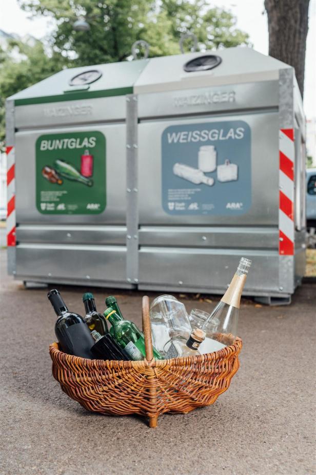 Ein Korb mit leeren Glasflaschen steht vor Containern für Buntglas und Weißglas.