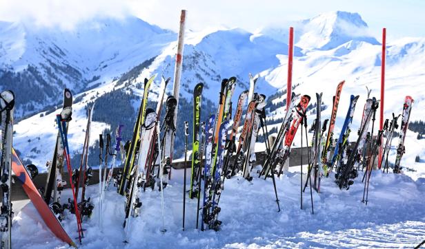Viele Skier und Skistöcke stehen im Schnee vor einer verschneiten Berglandschaft.