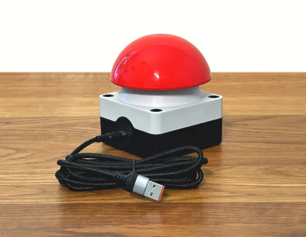 Großer USB-Buzzer mit rotem Knopf auf einem Holztisch.