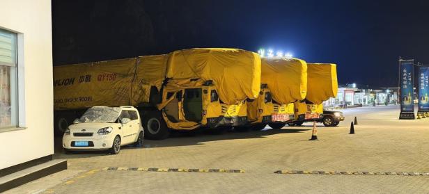 Mehrere Lkw mit gelben Planen und Zoomlion-Beschriftung stehen nachts auf einem Parkplatz.