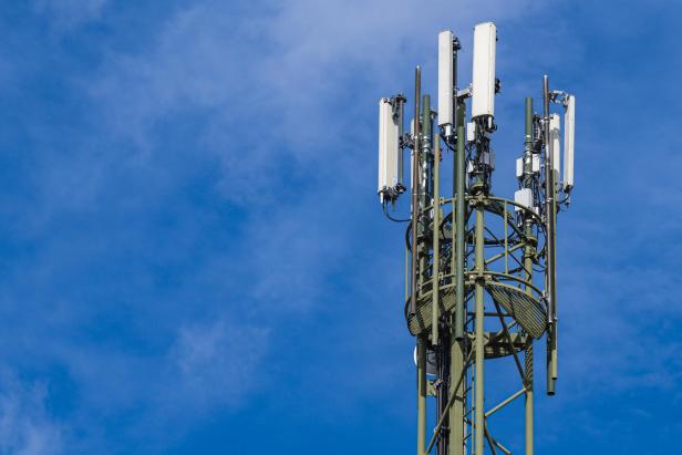 Mehrere Mobilfunkantennen sind an einem grünen Stahlmast vor blauem Himmel montiert.