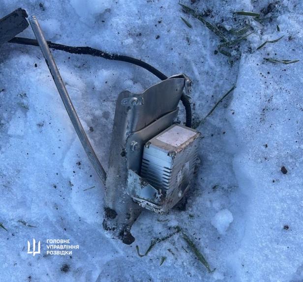 Metallisches Trümmerteil einer Drohne liegt im Schnee, umgeben von Gras und Erde.