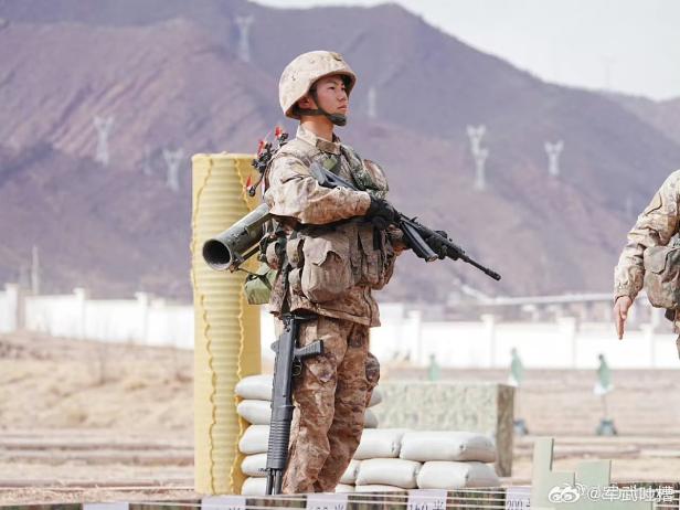 Chinesischer Soldat mit Sturmgewehr, Schrotflinte, Raketenwerfer und Drohne auf einem Übungsplatz.