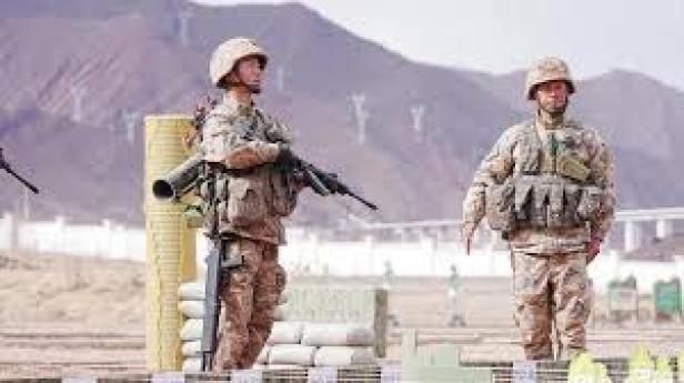 Ein chinesischer Soldat trägt Sturmgewehr, Schrotflinte, Raketenwerfer und Drohne bei einer Übung im Gebirge, während ein weiterer Soldat danebensteht.