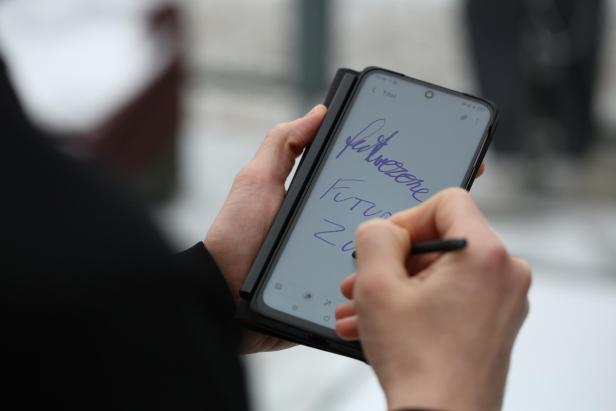 Person schreibt mit einem Stift handschriftliche Notizen auf ein Smartphone mit mattem Display.