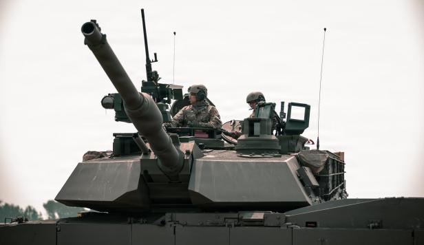 Zwei Soldaten sitzen auf einem Kampfpanzer mit großem Geschütz und Ausrüstung.