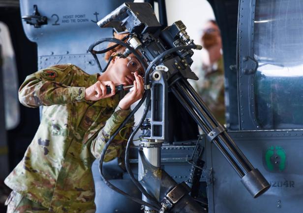Eine Soldatin wartet eine Minigun, die an einem Hubschrauber befestigt ist