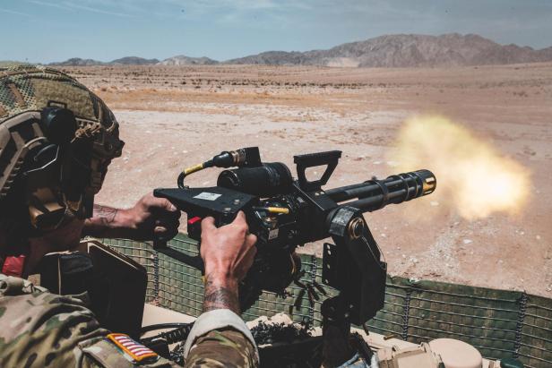 Ein US-Soldat feuert eine M134 Minigun mit rotierenden Läufen in einer Wüstenumgebung ab.