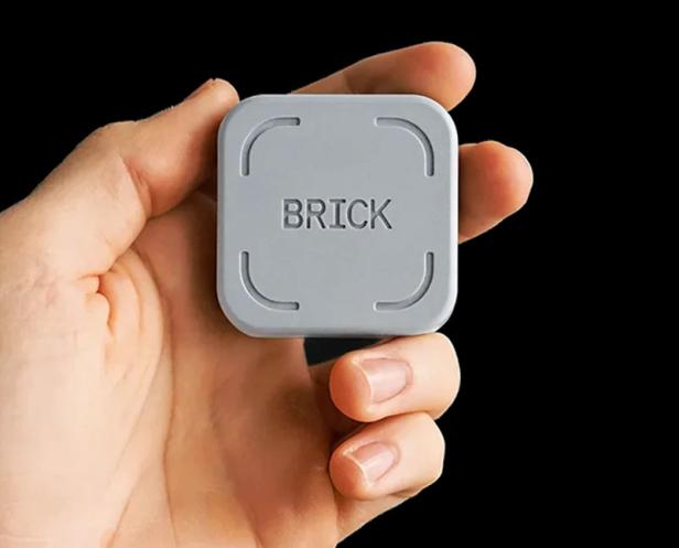 Grauer, quadratischer „Brick“-NFC-Block wird zwischen Daumen und Fingern gehalten.