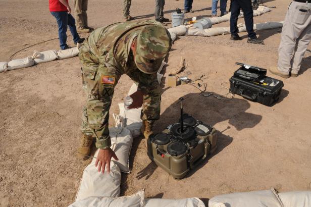 Soldat in Tarnuniform bereitet eine XM204-Mine auf sandigem Boden vor.