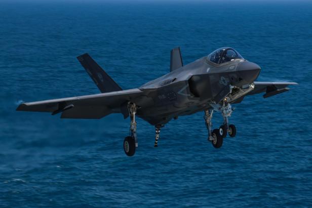 Eine F-35C der US Navy fliegt mit ausgefahrenem Fahrwerk über dem Meer und bereitet sich auf die Landung auf einem Flugzeugträger vor.