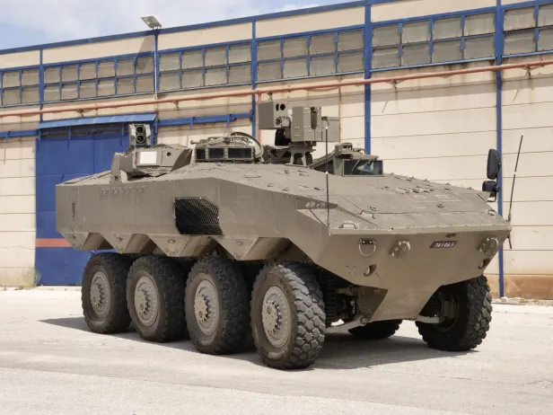 Ein Radpanzer steht vor einer Werkshalle