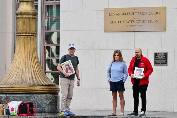 Drei Personen stehen vor einem Gerichtsgebäude, zwei halten gerahmte Fotos von jungen Menschen.