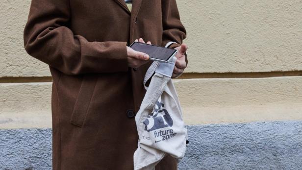 ein Mann im Mantel hält ein Smartphone an eine Einkaufstasche mit futurezone-Aufdruck