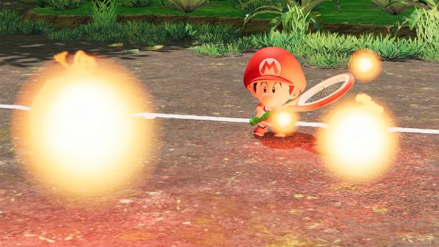 Baby-Mario mit Tennisschläger umgeben von leuchtenden Feuerbällen auf dem Tennisplatz.