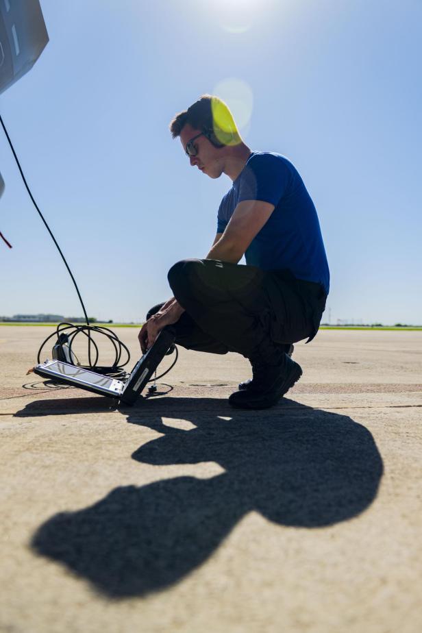 Techniker mit Headset arbeitet mit einem Laptop auf einem Flugfeld bei Sonnenschein.