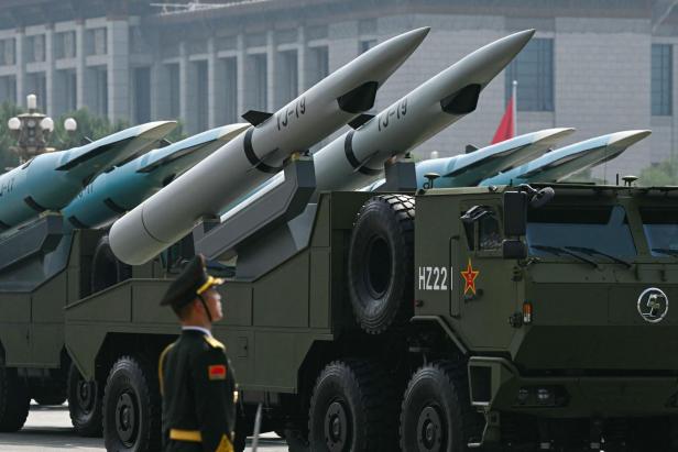 Mehrere Militärfahrzeuge mit Raketen und ein Soldat in Uniform stehen vor einem großen Gebäude.