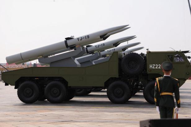 Militärfahrzeug mit mehreren großen Raketen, auf denen YJ-19 steht, und ein Soldat in Uniform im Vordergrund.