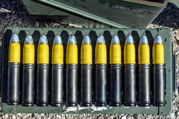 Mehrere 30-mm-Munitionen mit gelben Spitzen liegen nebeneinander in einer Munitionskiste.