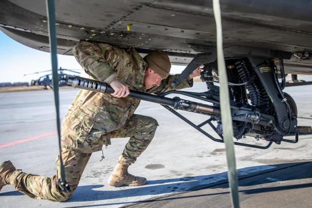 Soldat überprüft die M230-Kanone unter einem Apache-Kampfhubschrauber auf einem Flugfeld.
