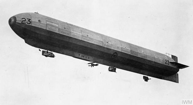 Zepplin mit Doppeldecker an der Unterseite fliegt vor grauem Himmel
