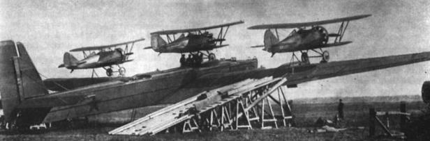 Drei Doppeldecker-Kampfflugzeuge sind auf den Tragflächen eines großen Bombers montiert.