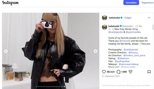 Frau mit Lederjacke hält eine Digitalkamera und fotografiert sich vor einem Spiegel.